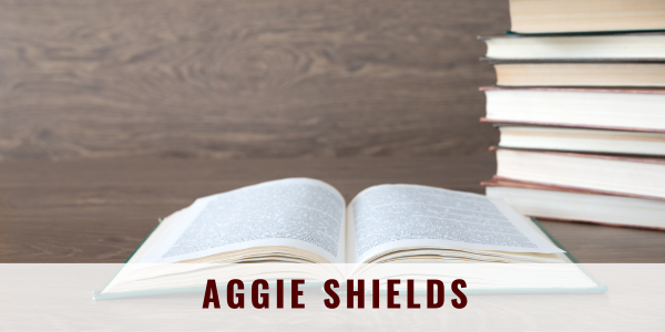 Open book on a desk with books piled to the right; "Aggie Shields" across the bottom.