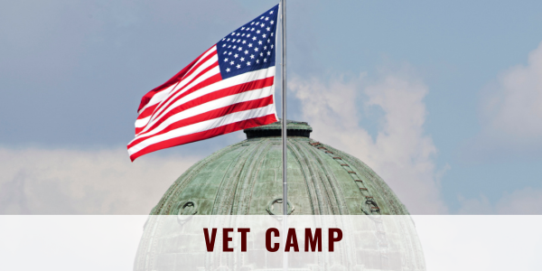 Dome of a building with a waving American flag on a pole. Words "Vet Camp" overlaid.